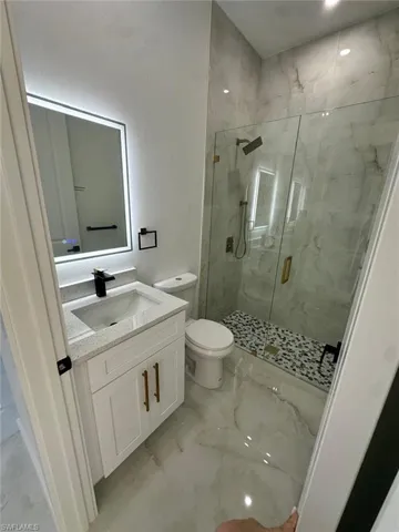 Bathroom featuring toilet, vanity, marble finish floor, and a marble finish shower