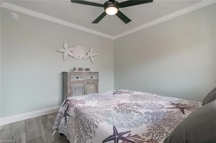 Bedroom featuring baseboards, crown molding, wood finished floors, and a ceiling fan
