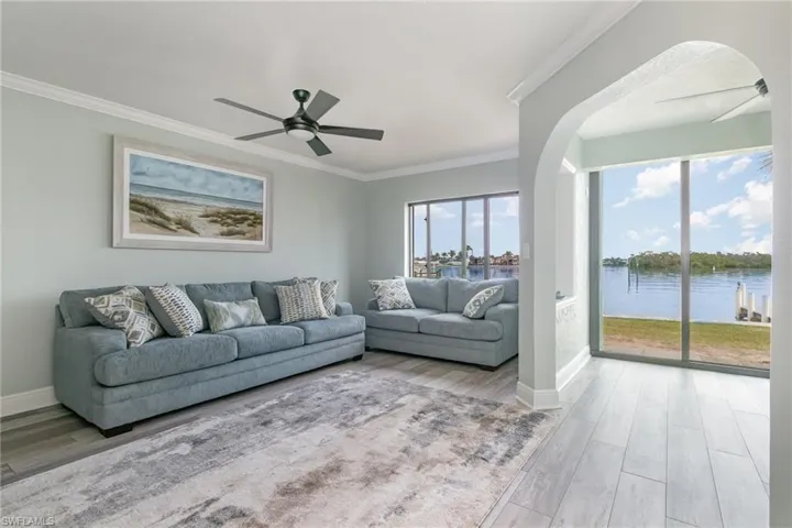 Living room with arched walkways, ceiling fan, ornamental molding, and a healthy amount of sunlight