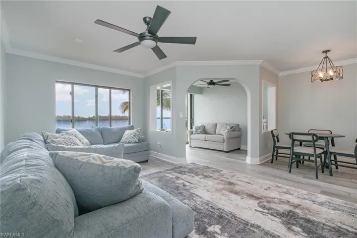 Living room featuring baseboards, ornamental molding, wood finished floors, arched walkways, and ceiling fan with notable chandelier