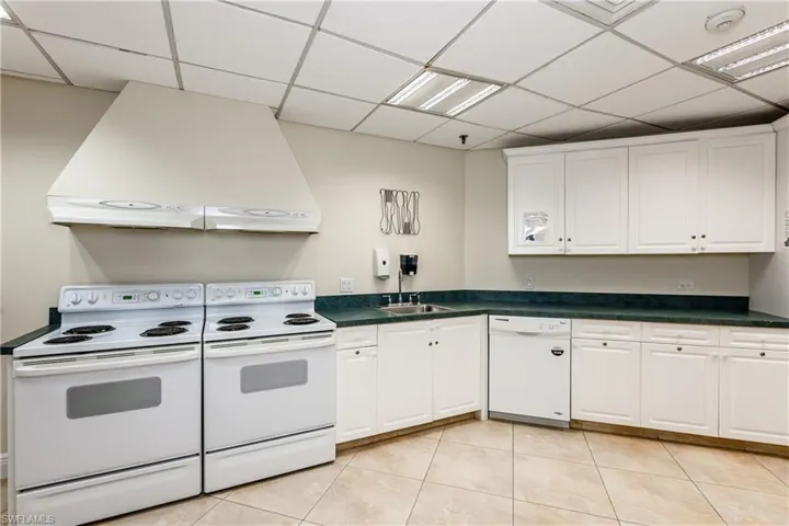 Kitchen with a paneled ceiling, white appliances, white cabinets, range hood, and dark countertops