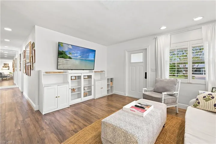Wood-finish flooring throughout, white built-in media cabinetry with glass-front display, recessed lighting, and a white entry door with frosted glass insert