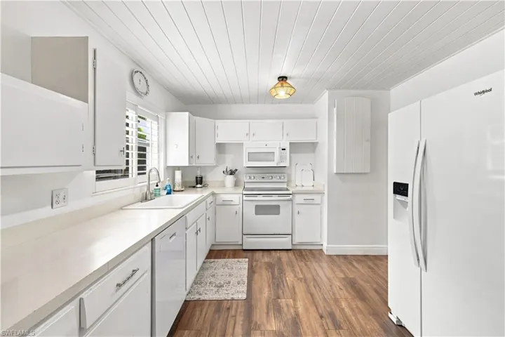 Kitchen featuring wood-finish flooring, white cabinetry, integrated appliances, light-toned countertops, and a white beadboard ceiling