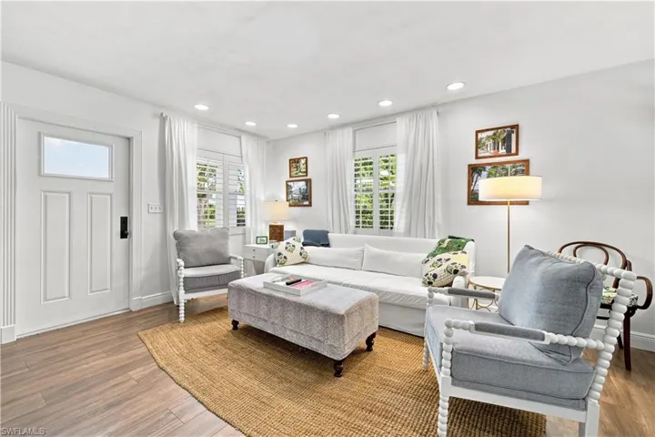 Recessed lighting, wood-finish flooring, white paneled door with transom window, window shutters, and ceiling-mounted light fixtures