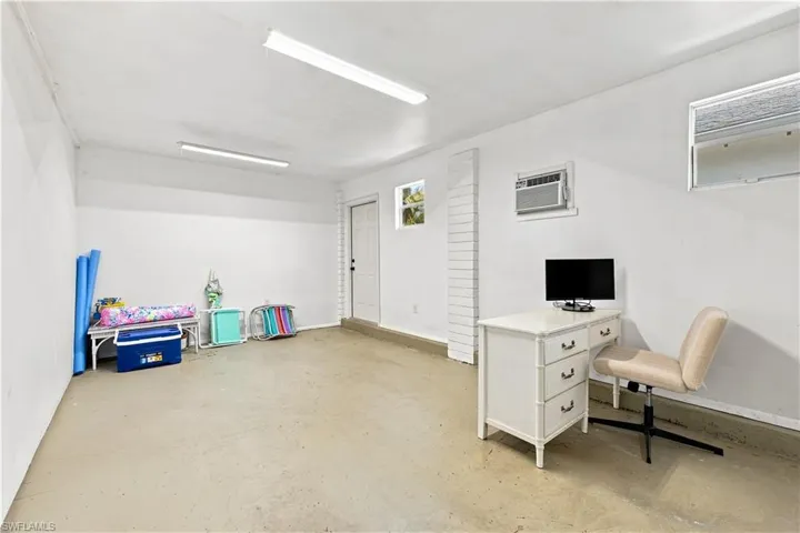 Bright, open room with concrete flooring, multiple windows, a wall-mounted air conditioning unit, and flush-mounted fluorescent lighting