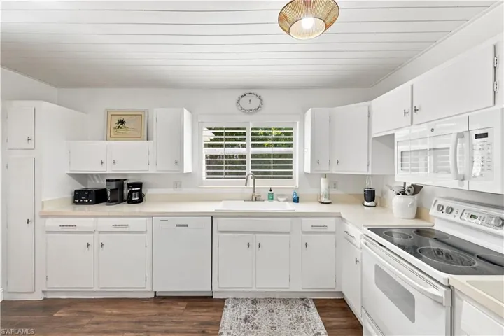 Efficient kitchen featuring ample white cabinetry, white appliances, and wood-finish flooring