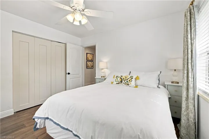 White paneled sliding closet doors, wood-finish flooring, white ceiling fan with integrated lighting, and an interior door with black hardware