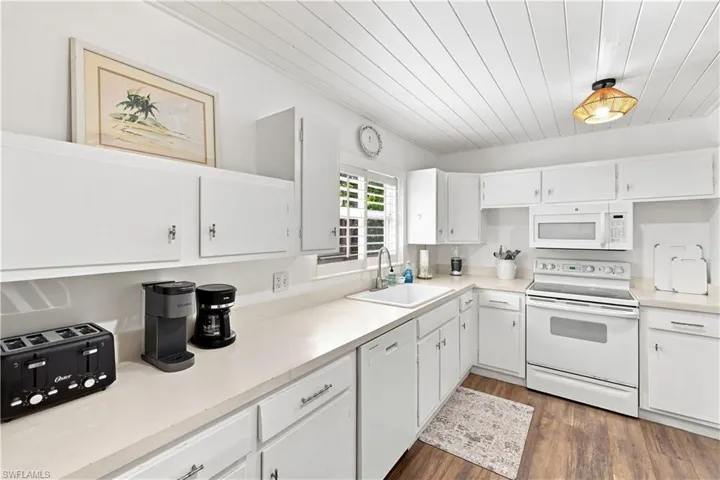 White cabinetry, wood-finish flooring, and white appliances in a corner kitchen layout