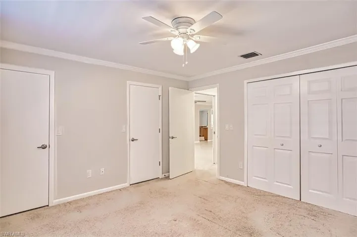 Unfurnished bedroom featuring light colored carpet, crown molding, and a ceiling fan