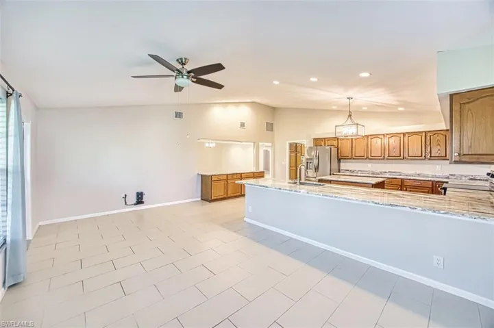 Kitchen featuring brown cabinetry, lofted ceiling, light stone countertops, stainless steel appliances, and hanging light fixtures