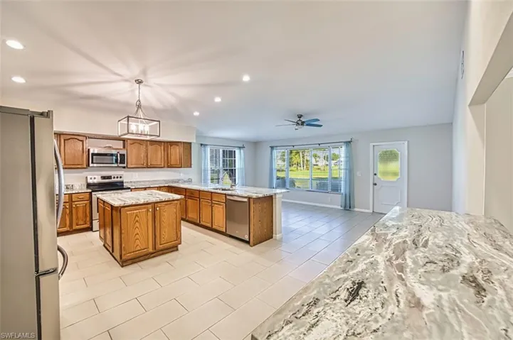 Kitchen featuring appliances with stainless steel finishes, brown cabinetry, recessed lighting, light stone countertops, and a peninsula