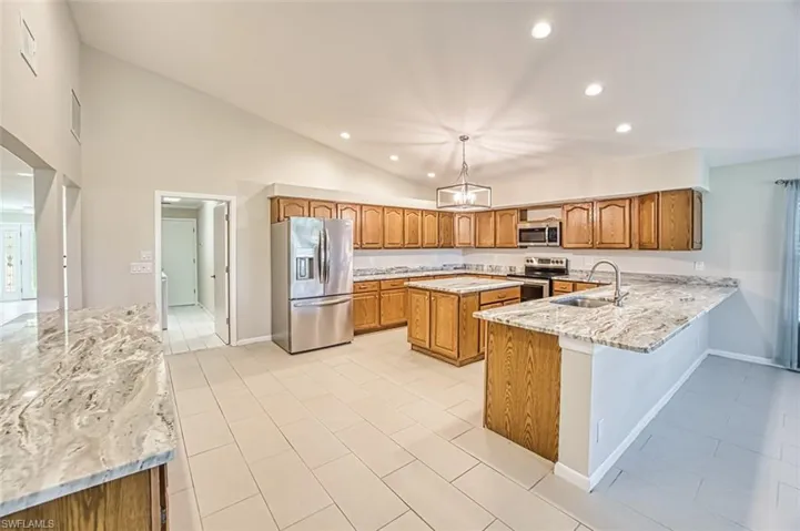 Kitchen featuring brown cabinetry, light stone counters, appliances with stainless steel finishes, recessed lighting, and a kitchen island