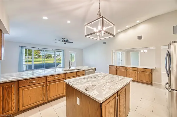 Kitchen with a peninsula, pendant lighting, lofted ceiling, brown cabinets, and appliances with stainless steel finishes