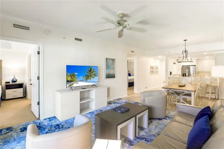 Living room with ceiling fan, light colored carpet, and ornamental molding