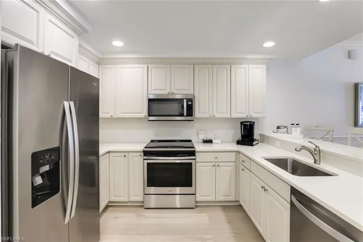 Kitchen with sink, white cabinets, light wood-type flooring, kitchen peninsula, and appliances with stainless steel finishes
