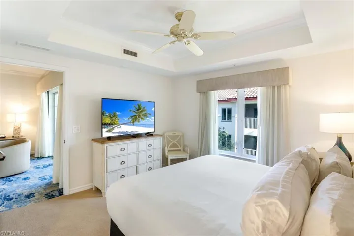 Carpeted bedroom featuring ceiling fan, crown molding, and a tray ceiling