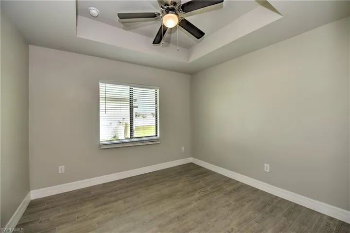 Empty room with hardwood / wood-style floors, ceiling fan, and a raised ceiling