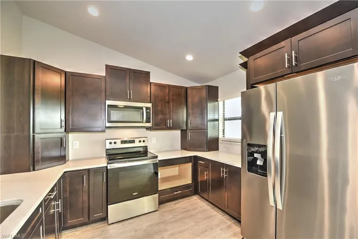 Kitchen featuring appliances with stainless steel finishes, lofted ceiling, dark brown cabinetry, and light hardwood / wood-style flooring