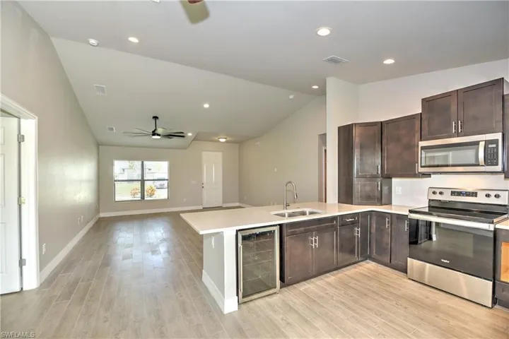 Kitchen with light wood-type flooring, appliances with stainless steel finishes, wine cooler, sink, and ceiling fan