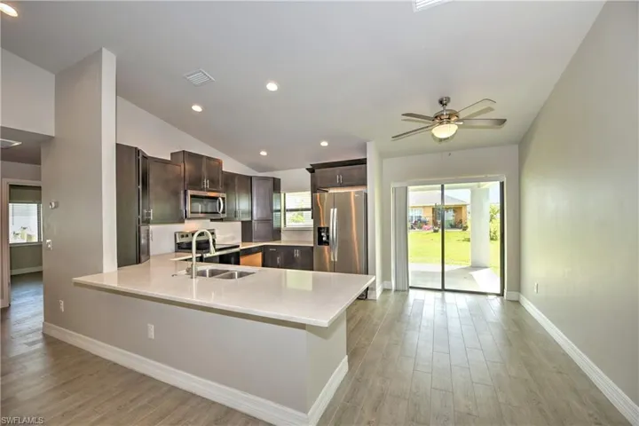 Kitchen with lofted ceiling, light wood-type flooring, appliances with stainless steel finishes, sink, and ceiling fan