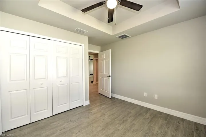 Unfurnished bedroom with ceiling fan, a raised ceiling, a closet, and wood-type flooring