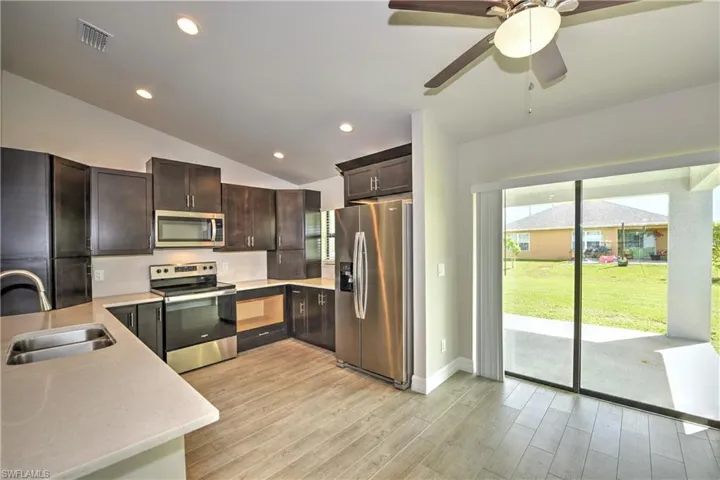 Kitchen with ceiling fan, light hardwood / wood-style floors, stainless steel appliances, vaulted ceiling, and sink