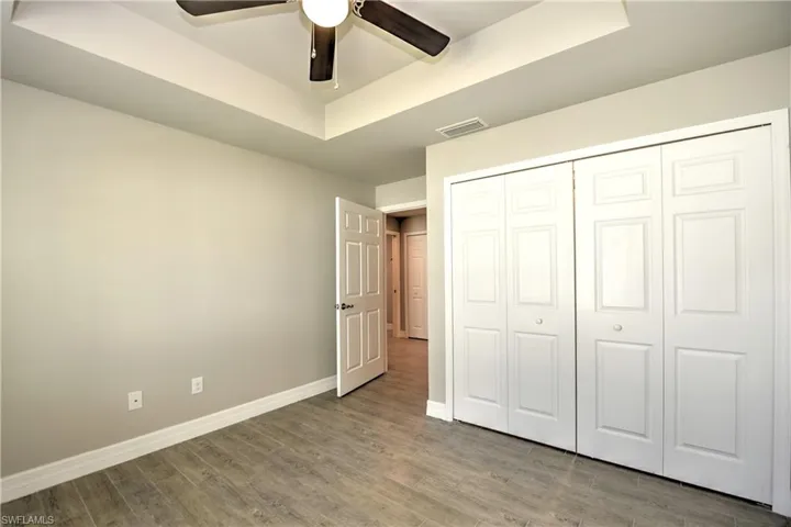 Unfurnished bedroom with hardwood / wood-style floors, a closet, ceiling fan, and a raised ceiling