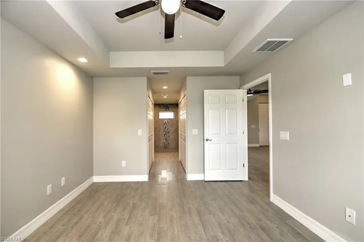Unfurnished bedroom featuring a raised ceiling, ceiling fan, and light hardwood / wood-style floors