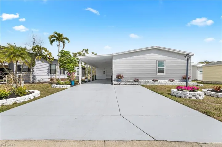 Manufactured / mobile home featuring a carport, concrete driveway, a front yard, and a patio area