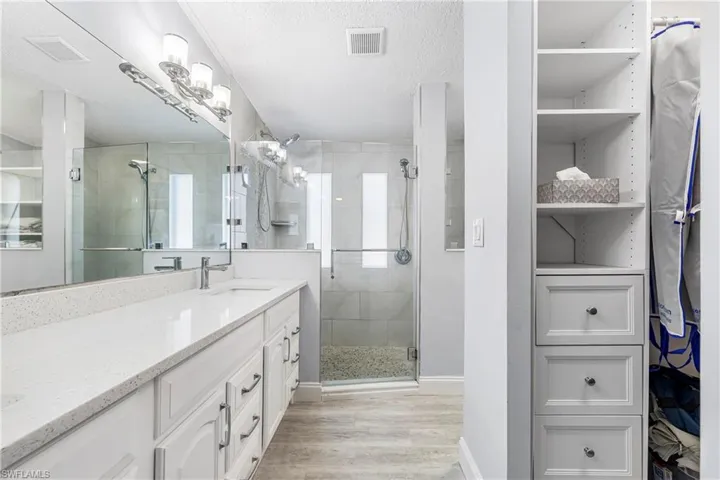 Bathroom featuring a shower stall, a textured ceiling, vanity, a closet, and light wood-style flooring