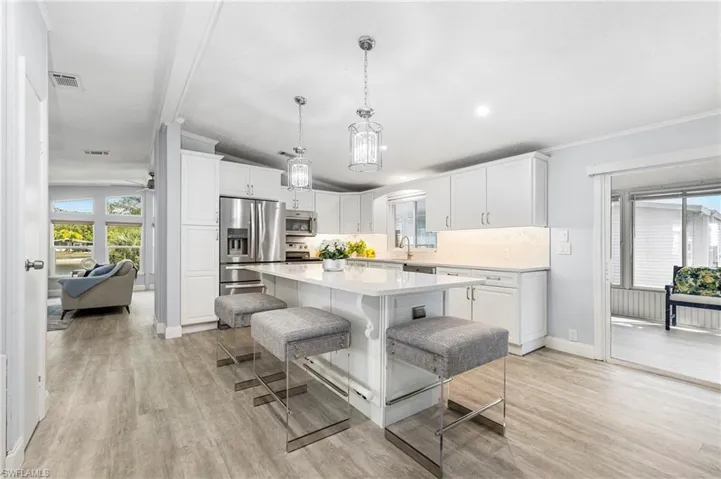 Kitchen featuring white cabinetry, stainless steel appliances, light wood-style floors, ornamental molding, quartz countertops and a breakfast bar