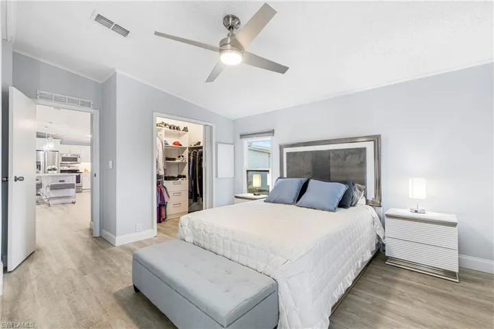Bedroom featuring light wood finished floors, crown molding, a spacious closet, stainless steel fridge, and ceiling fan