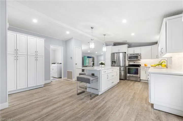 Kitchen with a breakfast bar, white cabinetry, stainless steel appliances, a center island, quartz countertops and decorative light fixtures
