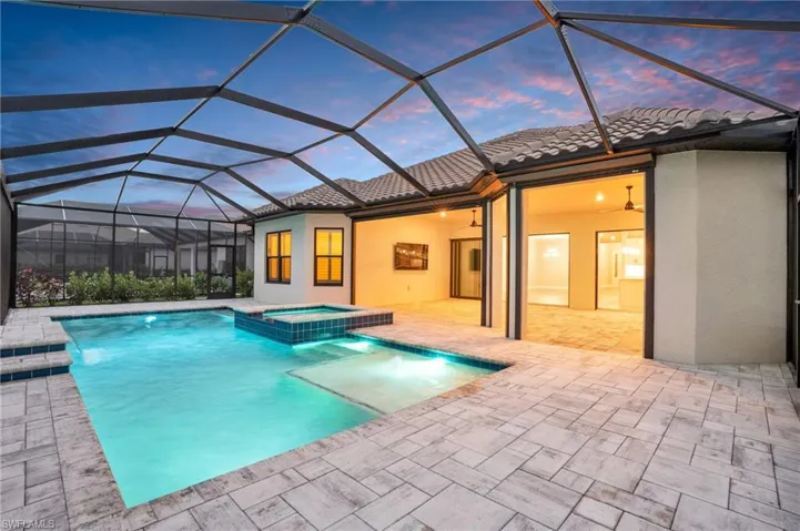 Pool at dusk featuring a patio, a lanai, pool water feature, and an in ground hot tub