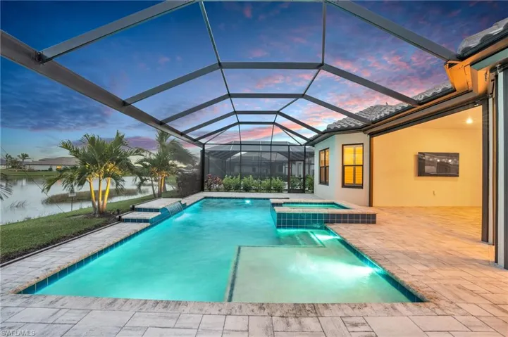 Pool at dusk featuring an in ground hot tub, a patio, pool water feature, a water view, and a lanai