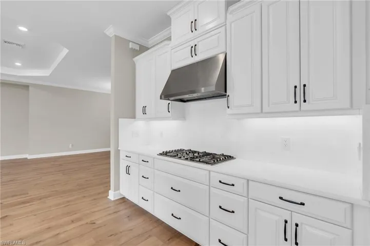 Kitchen with white cabinets, light hardwood / wood-style flooring, stainless steel gas stovetop, and crown molding