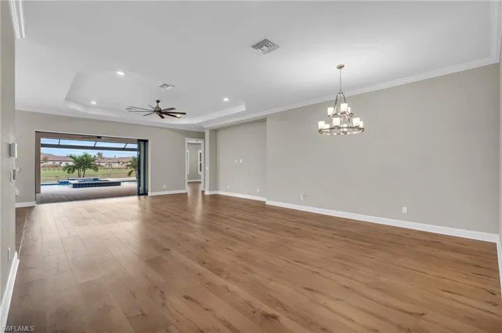 Unfurnished living room with hardwood / wood-style floors, ceiling fan with notable chandelier, ornamental molding, and a tray ceiling