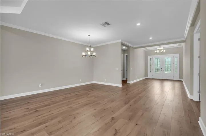 Unfurnished living room featuring ornamental molding, light wood-type flooring, a notable chandelier, and french doors