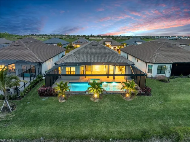 Back house at dusk with a lanai, a lawn, and a patio