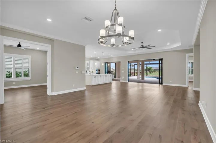 Unfurnished living room with hardwood / wood-style floors, ornamental molding, and ceiling fan with notable chandelier