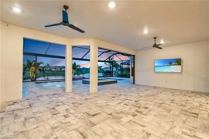 Patio terrace at dusk featuring a pool with hot tub, ceiling fan, glass enclosure, and a water view