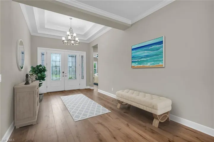 Foyer entrance with light hardwood / wood-style floors, an inviting chandelier, a raised ceiling, crown molding, and french doors