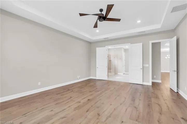 Unfurnished bedroom featuring light wood-type flooring, ceiling fan, and a tray ceiling