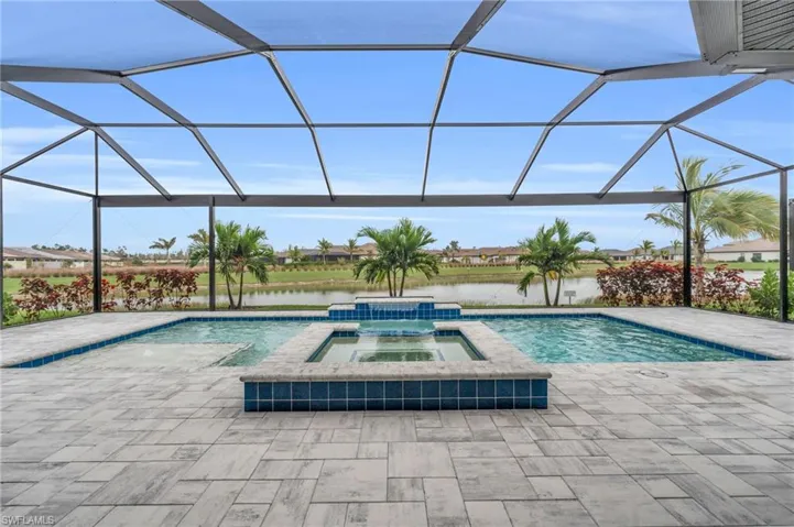 View of swimming pool featuring a lanai, a water view, a patio, and an in ground hot tub