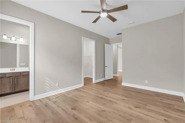 Unfurnished bedroom with light wood-type flooring, ensuite bath, ceiling fan, and a walk in closet