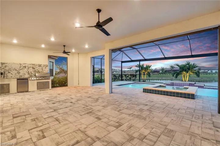 Patio terrace at dusk with an outdoor kitchen, a grill, a swimming pool with hot tub, a lanai, and ceiling fan