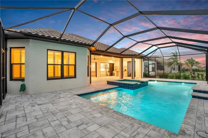 Pool at dusk featuring a patio, a lanai, and an in ground hot tub