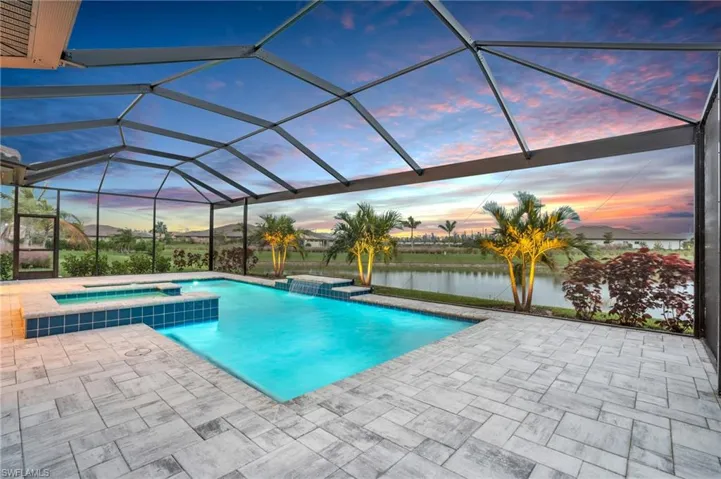 Pool at dusk with glass enclosure, a patio area, a water view, and an in ground hot tub