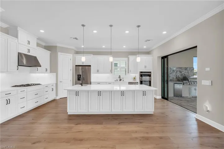 Kitchen with light wood-type flooring, decorative light fixtures, and an island with sink