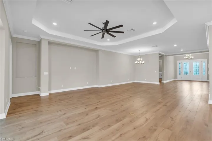 Unfurnished living room with ornamental molding, ceiling fan with notable chandelier, light hardwood / wood-style floors, and a raised ceiling